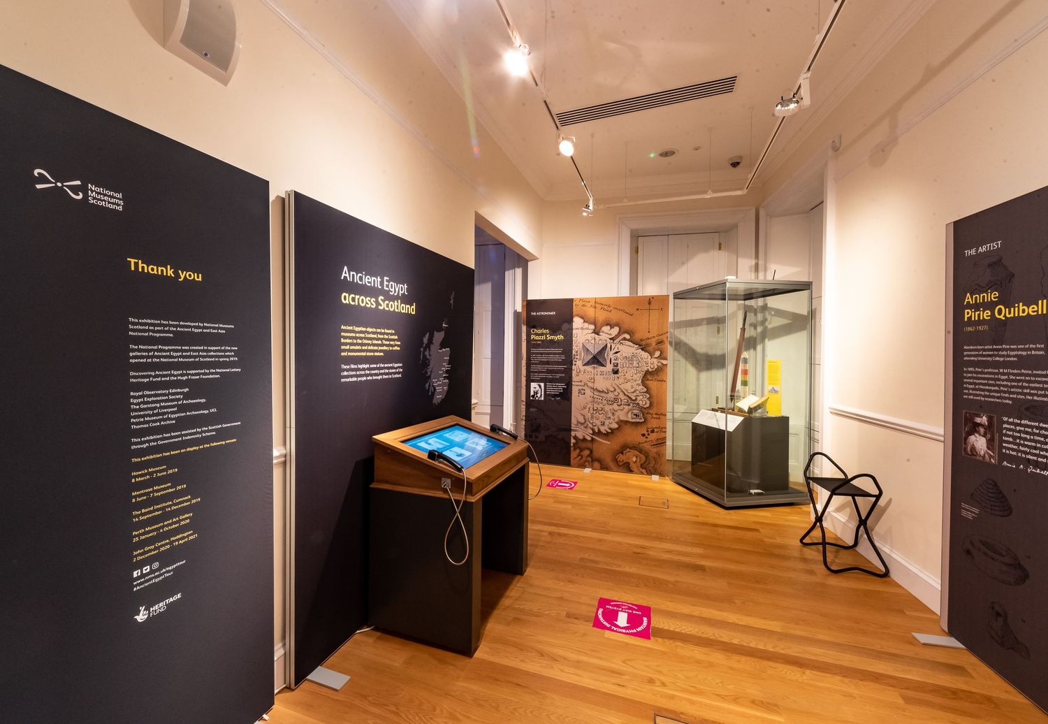 Exhibition space with interactive displays and informational panels along cream-colored walls.