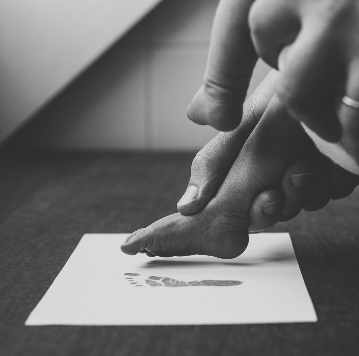 Close up of baby foot and adult hands, creating footprint on paper