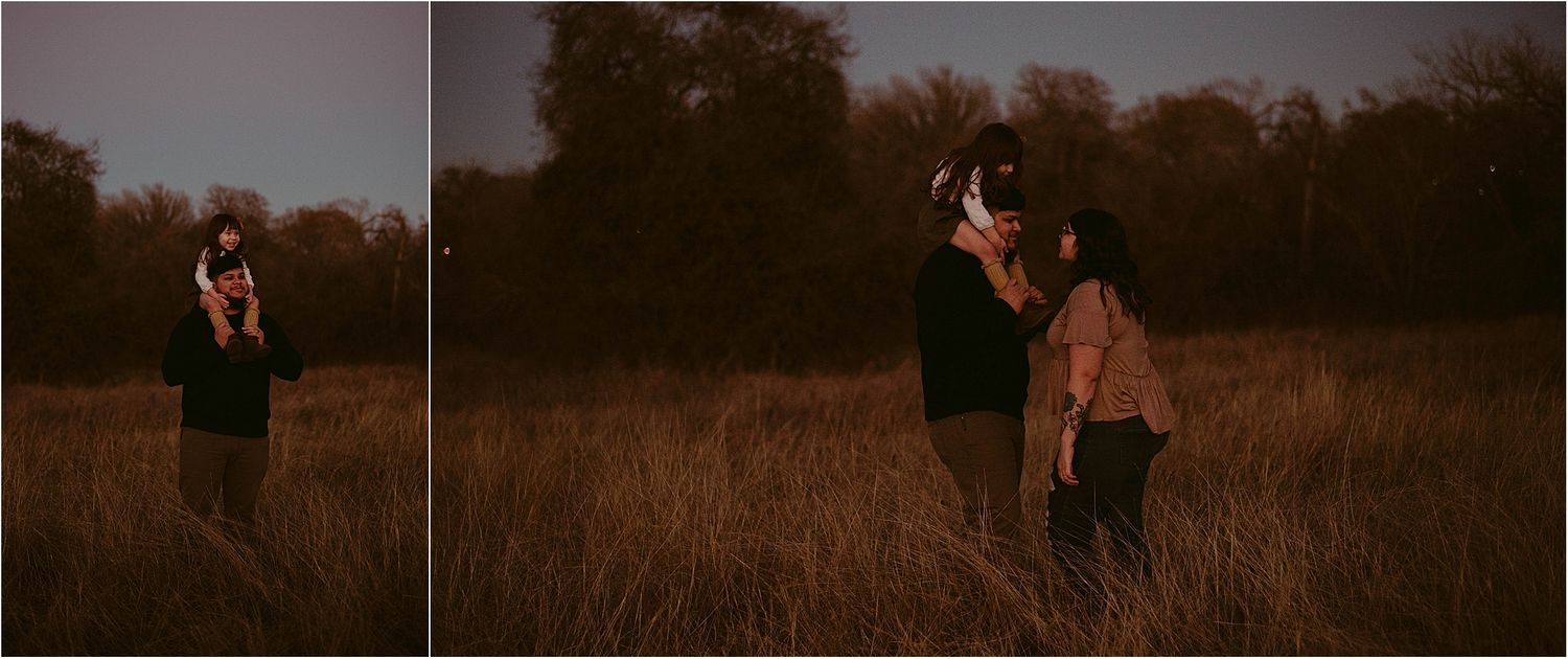 Two silhouettes stand in a golden field at dusk with tall grass and trees in the background.