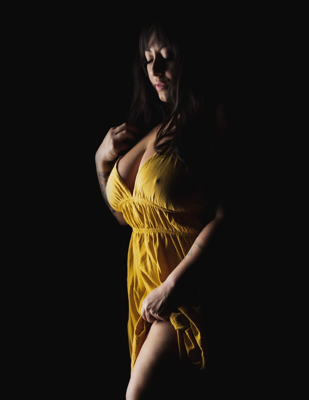 A person in a flowing yellow dress poses dramatically against a dark background in moody lighting.
