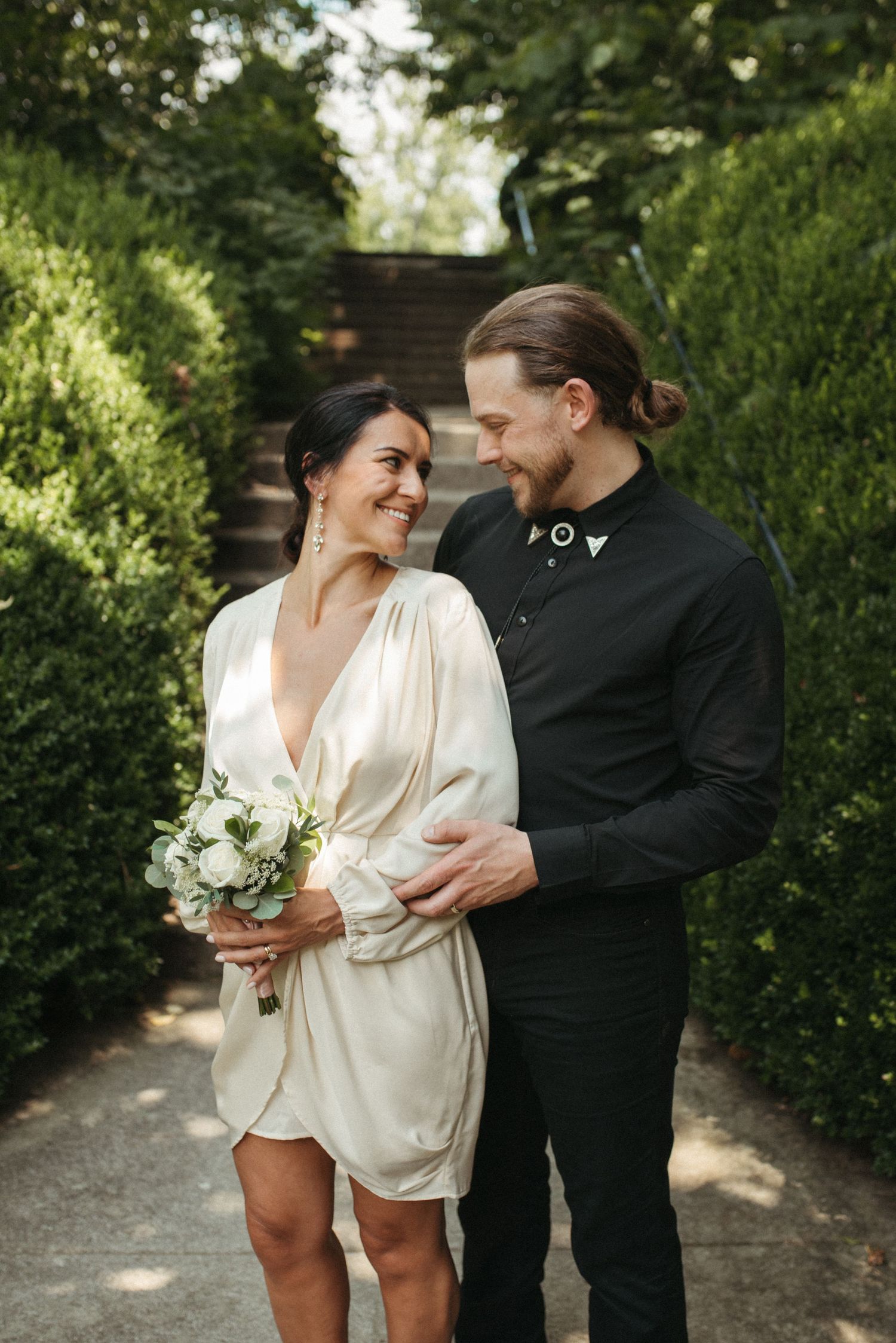 A loving moment captured between a couple on a garden path surrounded by green hedges.
