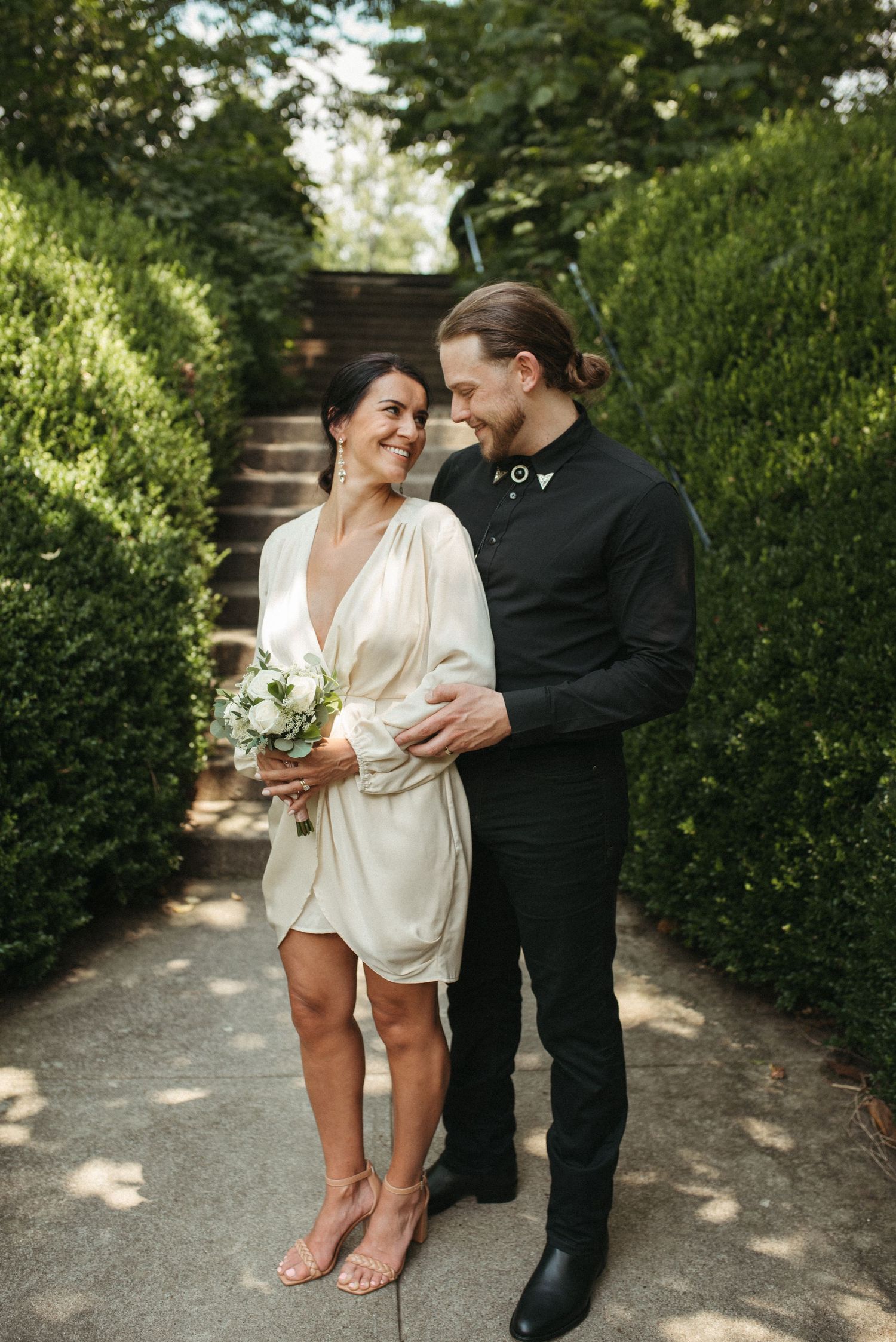 A couple shares an intimate moment on a garden path lined with perfectly trimmed hedges.