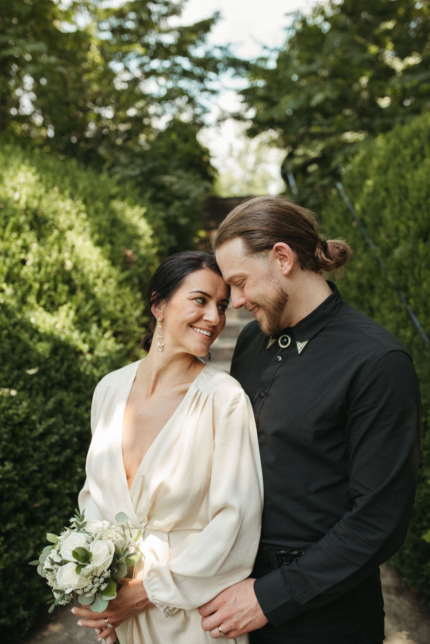 A tender moment between a couple on a garden path with lush green hedges and natural lighting.