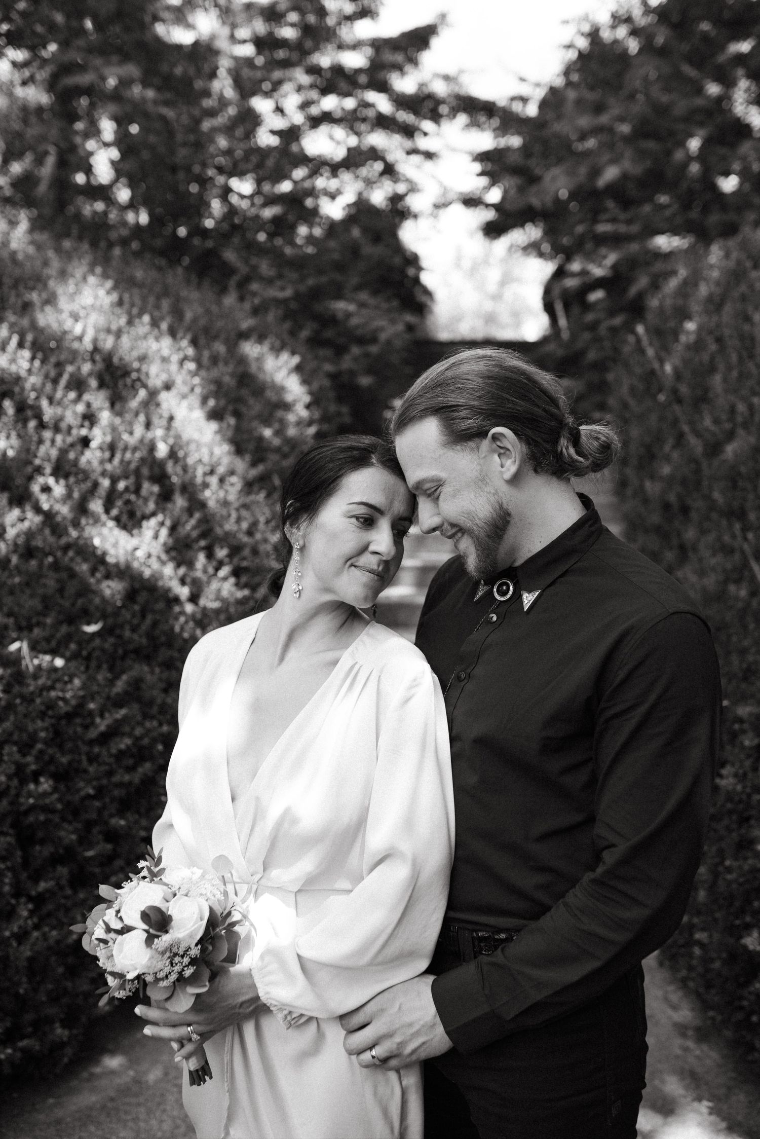 A romantic black and white wedding photo of a couple in a garden with the bride holding a bouquet.