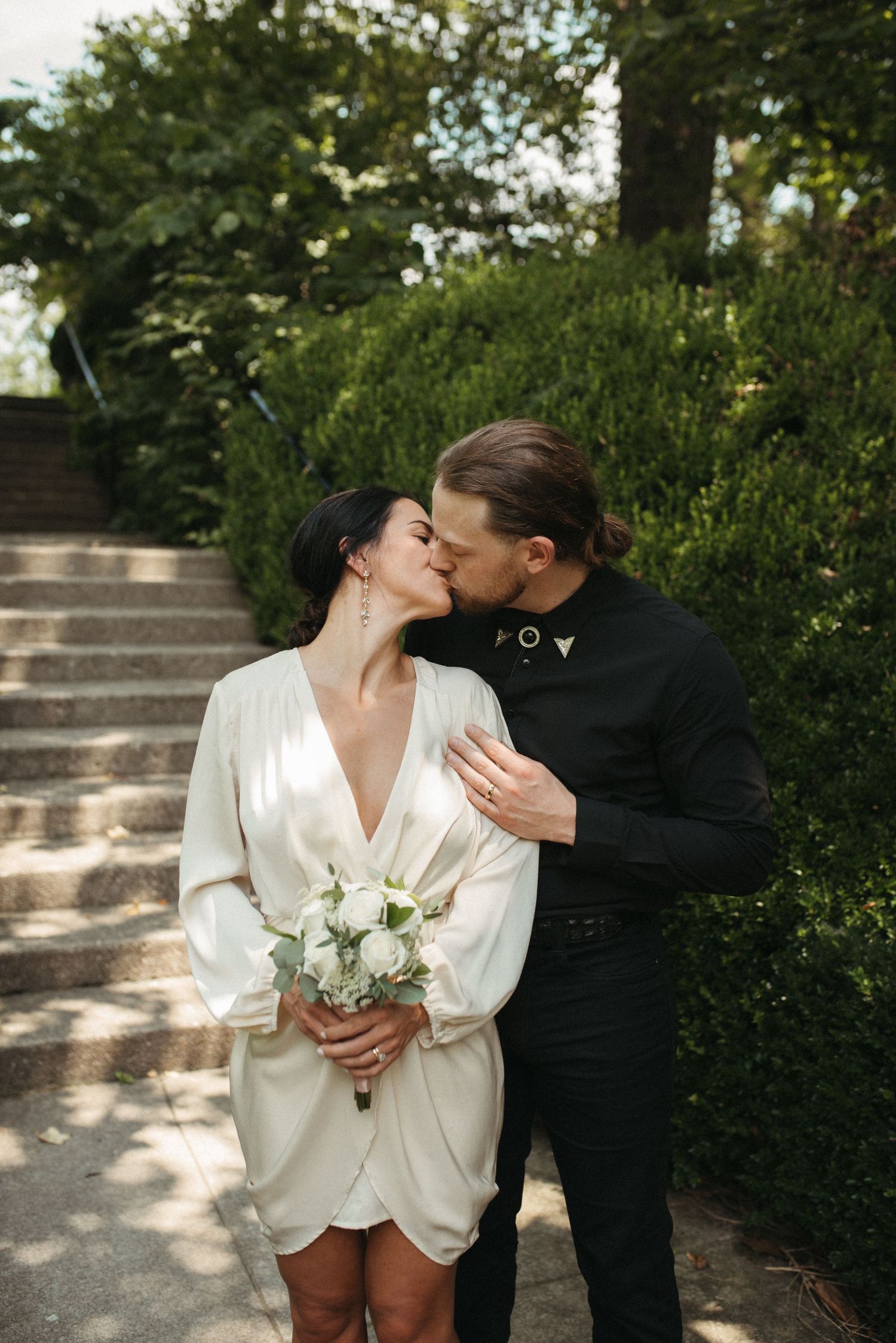 A romantic wedding photo on garden steps with the bride in white and groom in black sharing a kiss.