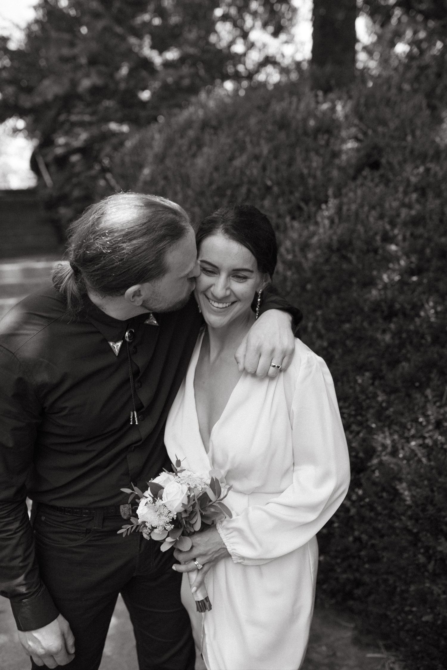 A black and white candid wedding photo capturing a tender moment between the couple.