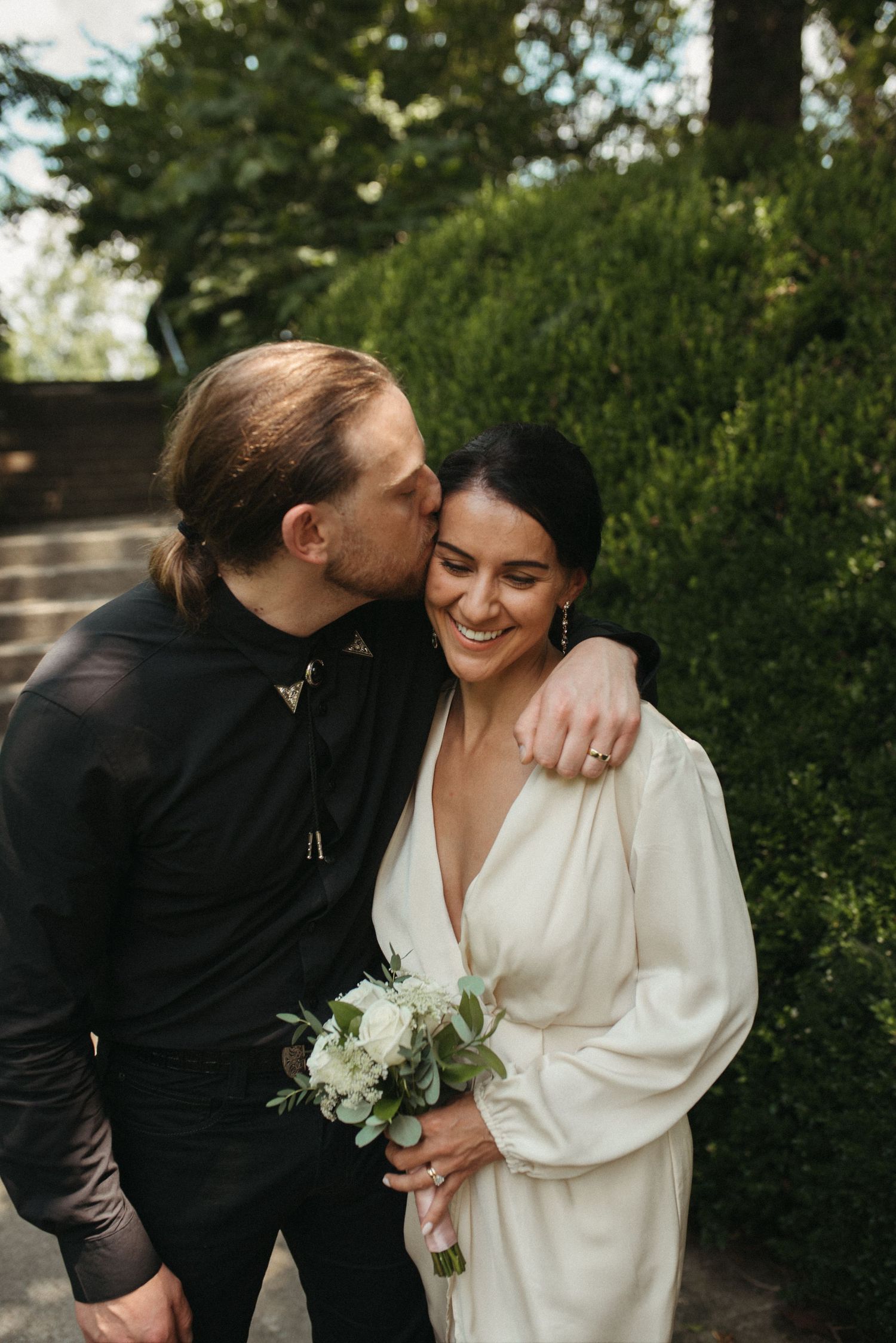 A joyful wedding portrait with the couple sharing laughter in a garden setting.