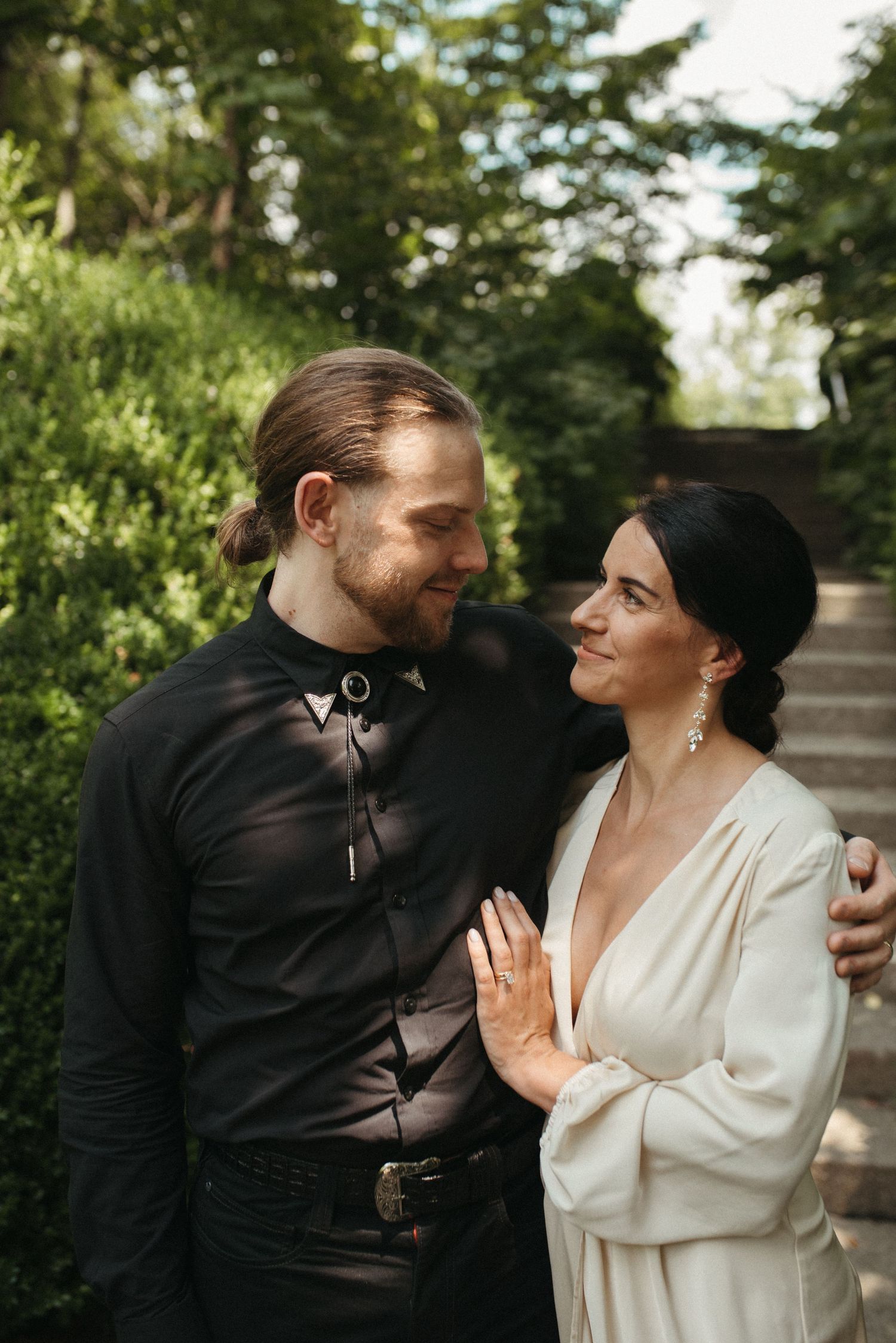 A couple in wedding attire share an intimate moment on a garden path surrounded by greenery.