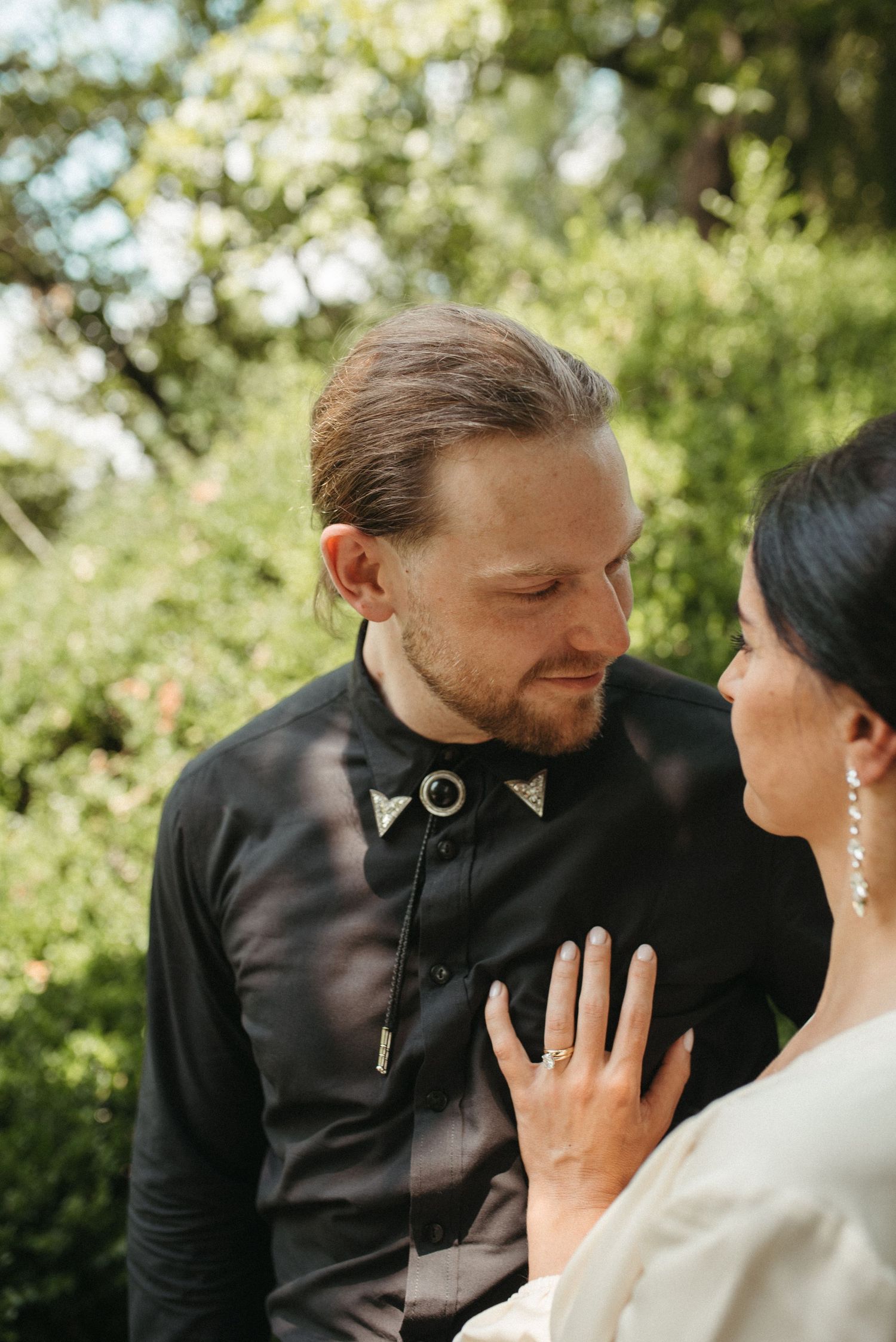 A romantic couple in contrasting black and white outfits share a tender moment in dappled sunlight.