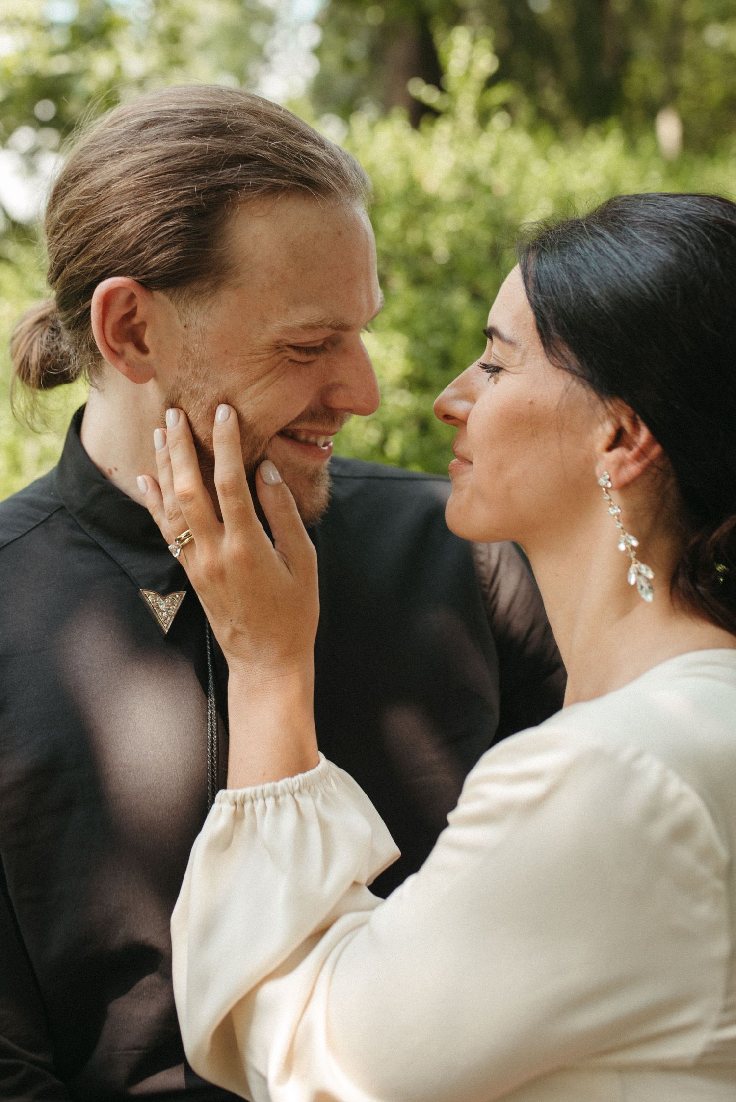 A loving couple shares an intimate moment as she touches his face while wearing elegant attire.