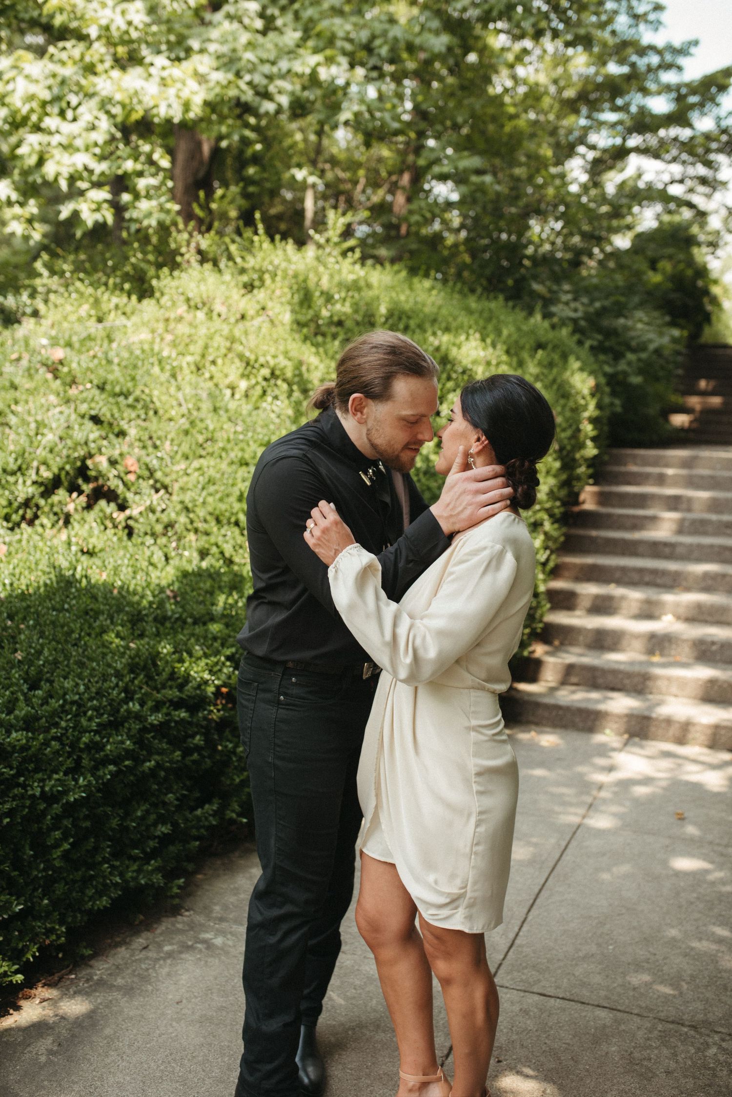 A romantic couple shares an intimate moment on outdoor stone steps surrounded by lush greenery.