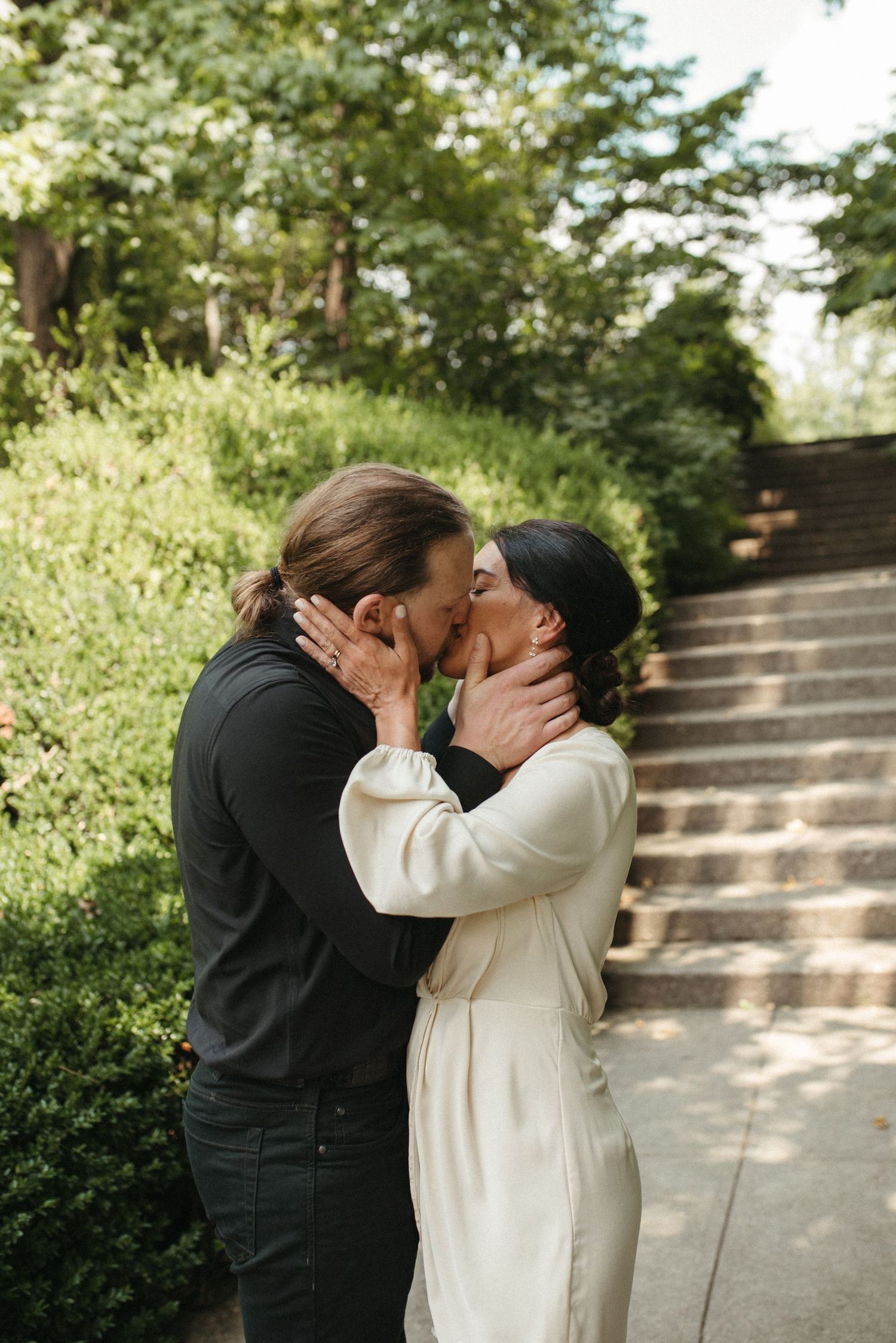 Couple embracing in a tender moment on a garden pathway with stone steps in the background.