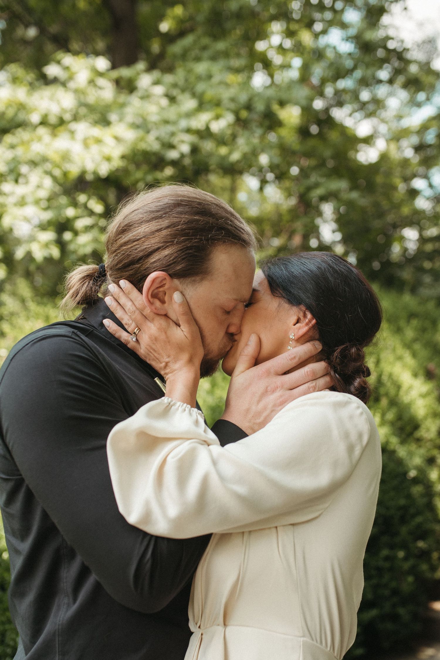A passionate embrace between two people in formal attire against a sunlit garden backdrop.