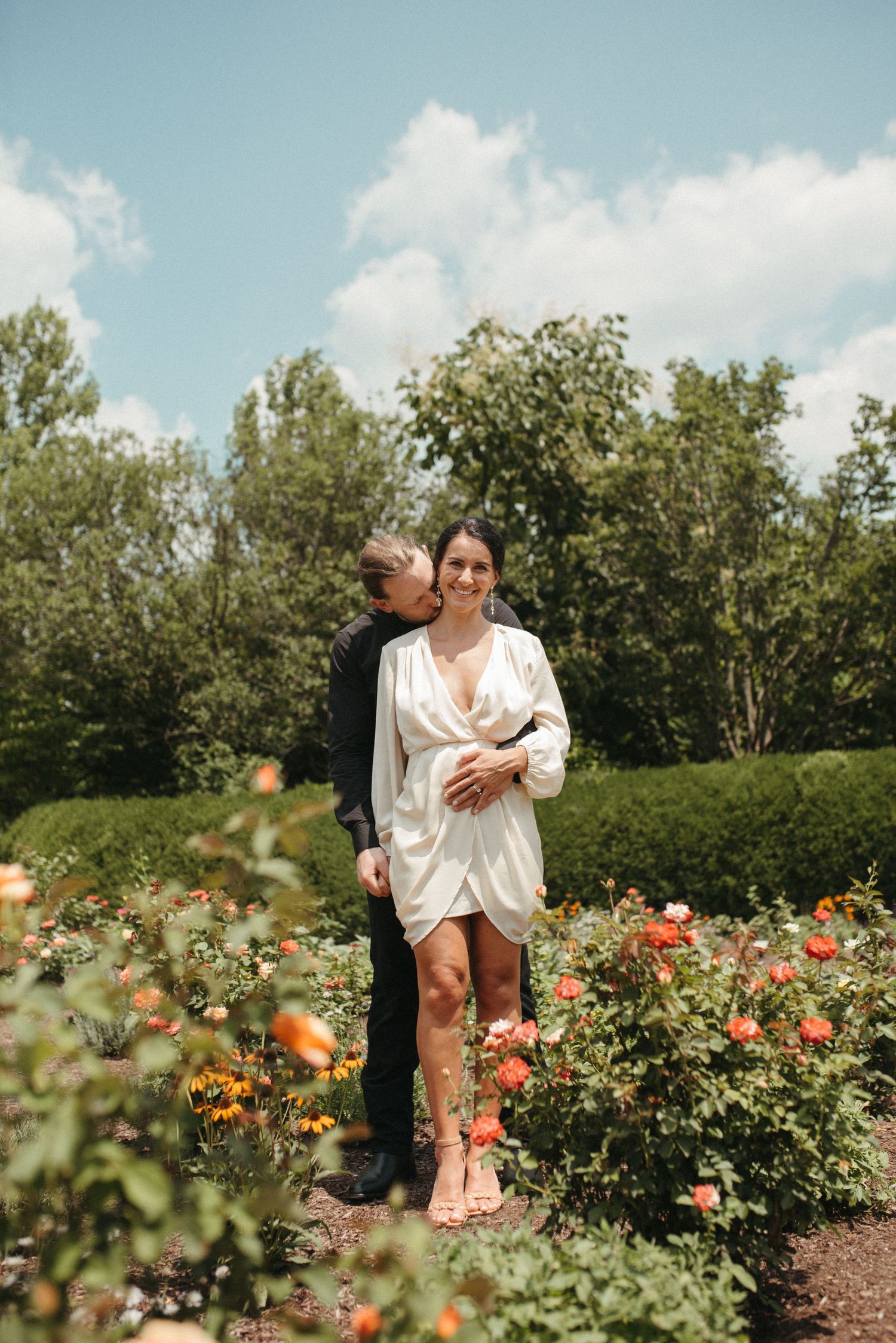 Couple standing together in a blooming rose garden on a sunny summer day.