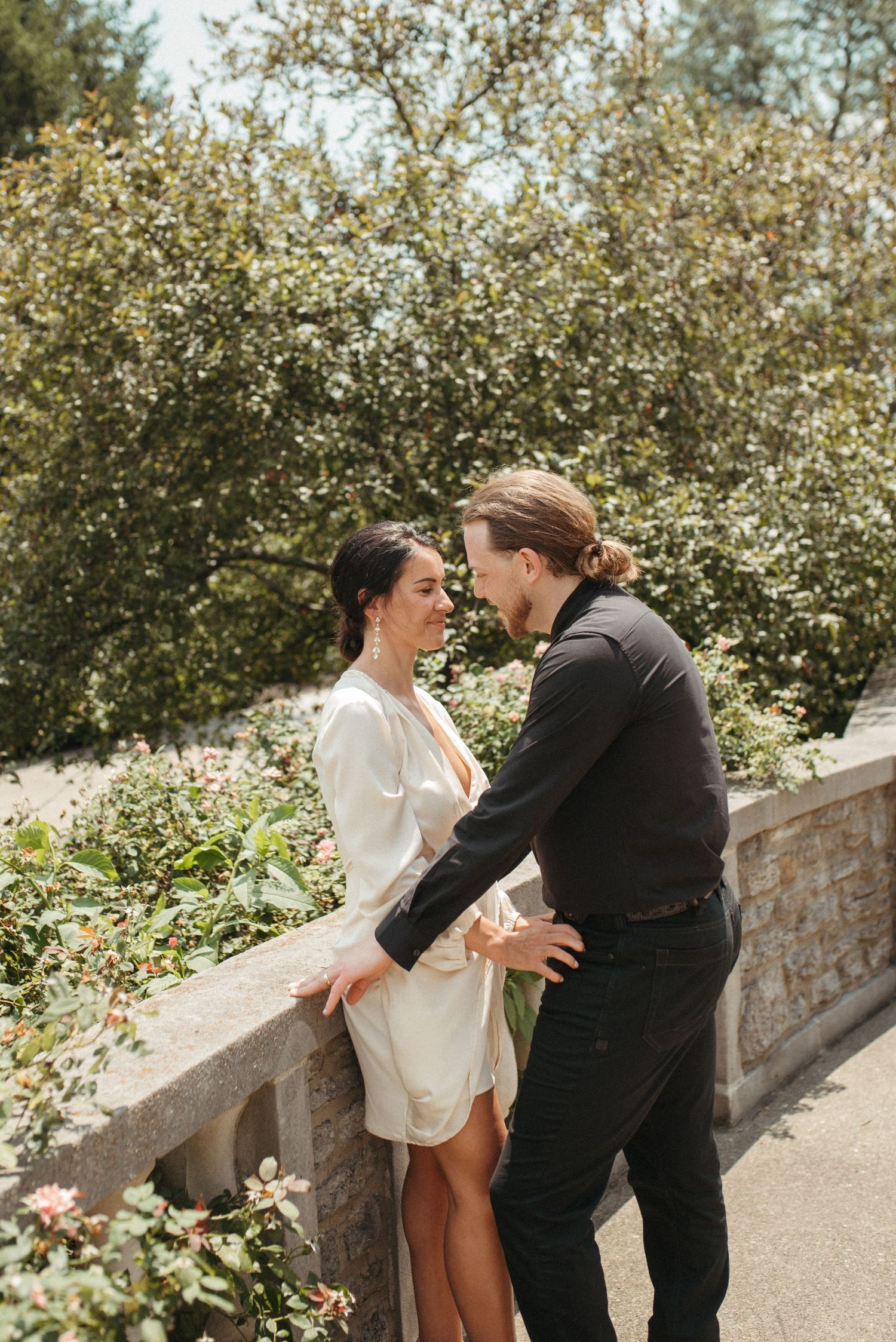 A couple shares a romantic moment on a stone pathway surrounded by flowering bushes.