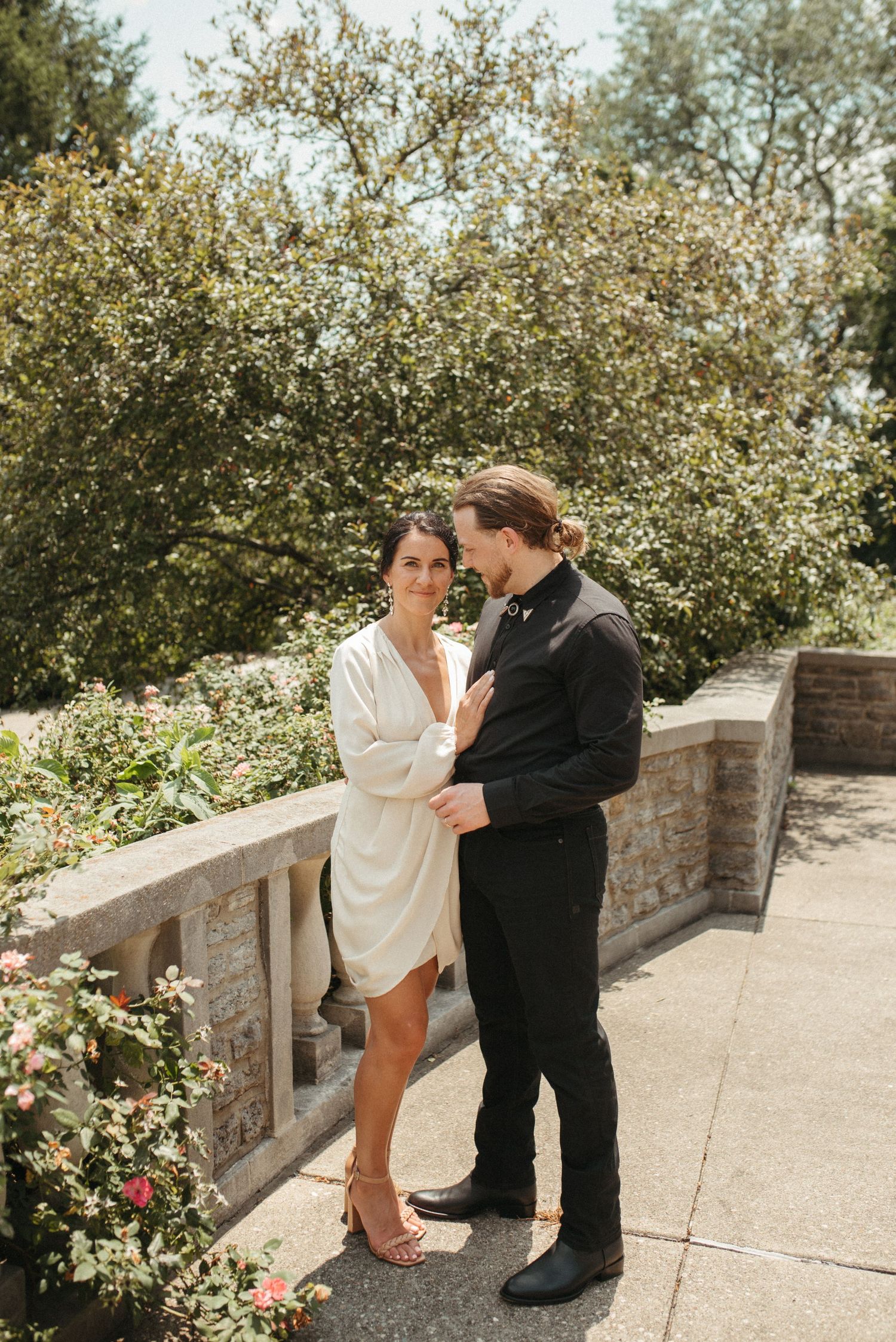 Couple in contrasting black and white outfits standing together on a garden terrace.