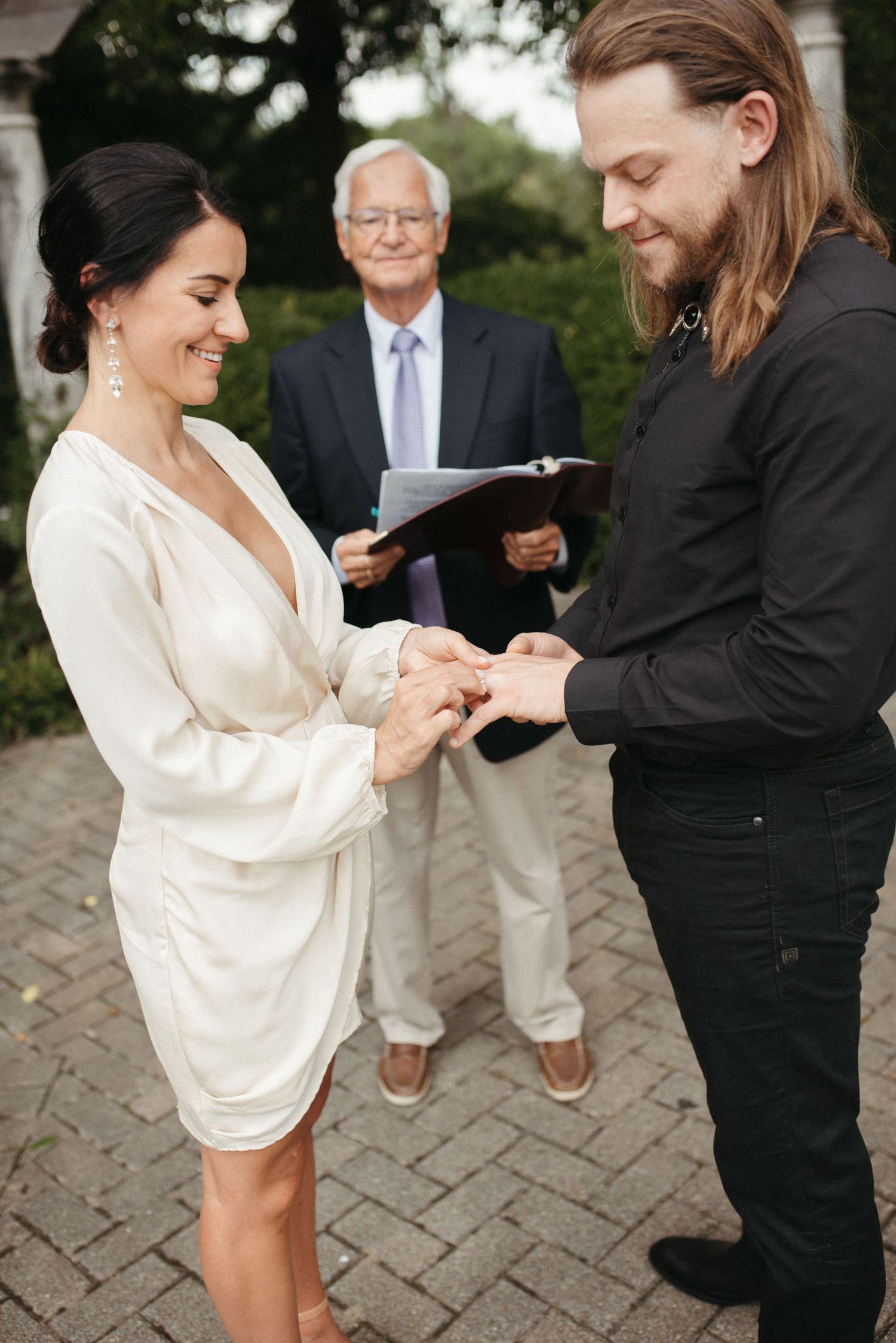 An exchange of rings during an intimate garden wedding ceremony beneath a stone pergola.