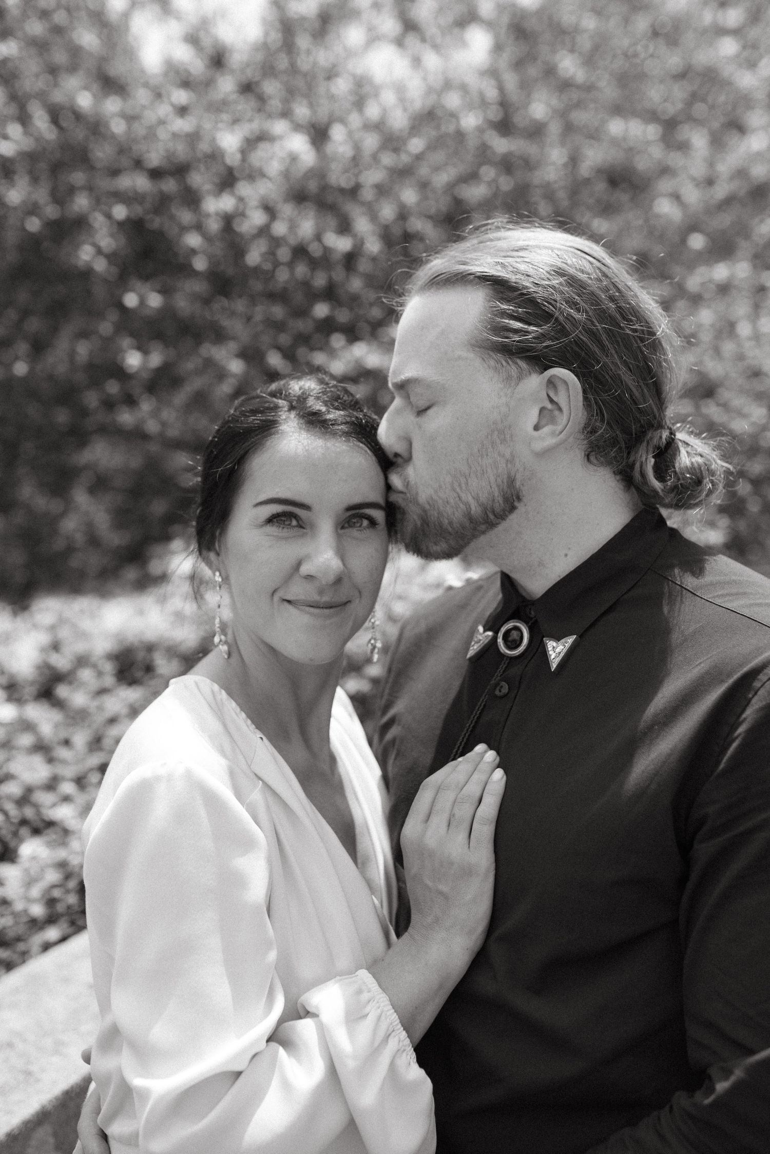Black and white portrait of a couple showing affection in an outdoor garden setting.