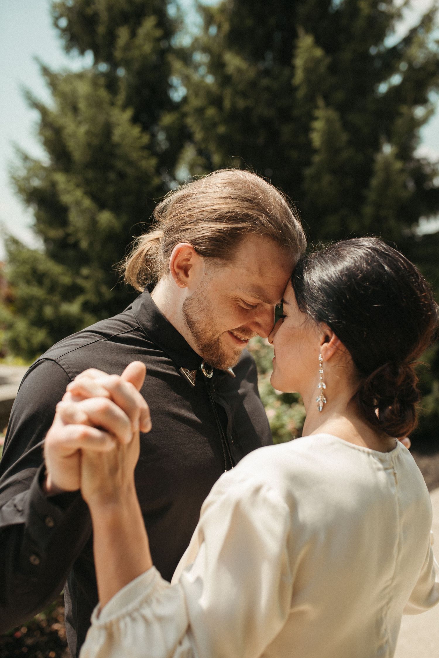 A couple sharing a romantic dance pose outdoors with evergreen trees in the background.