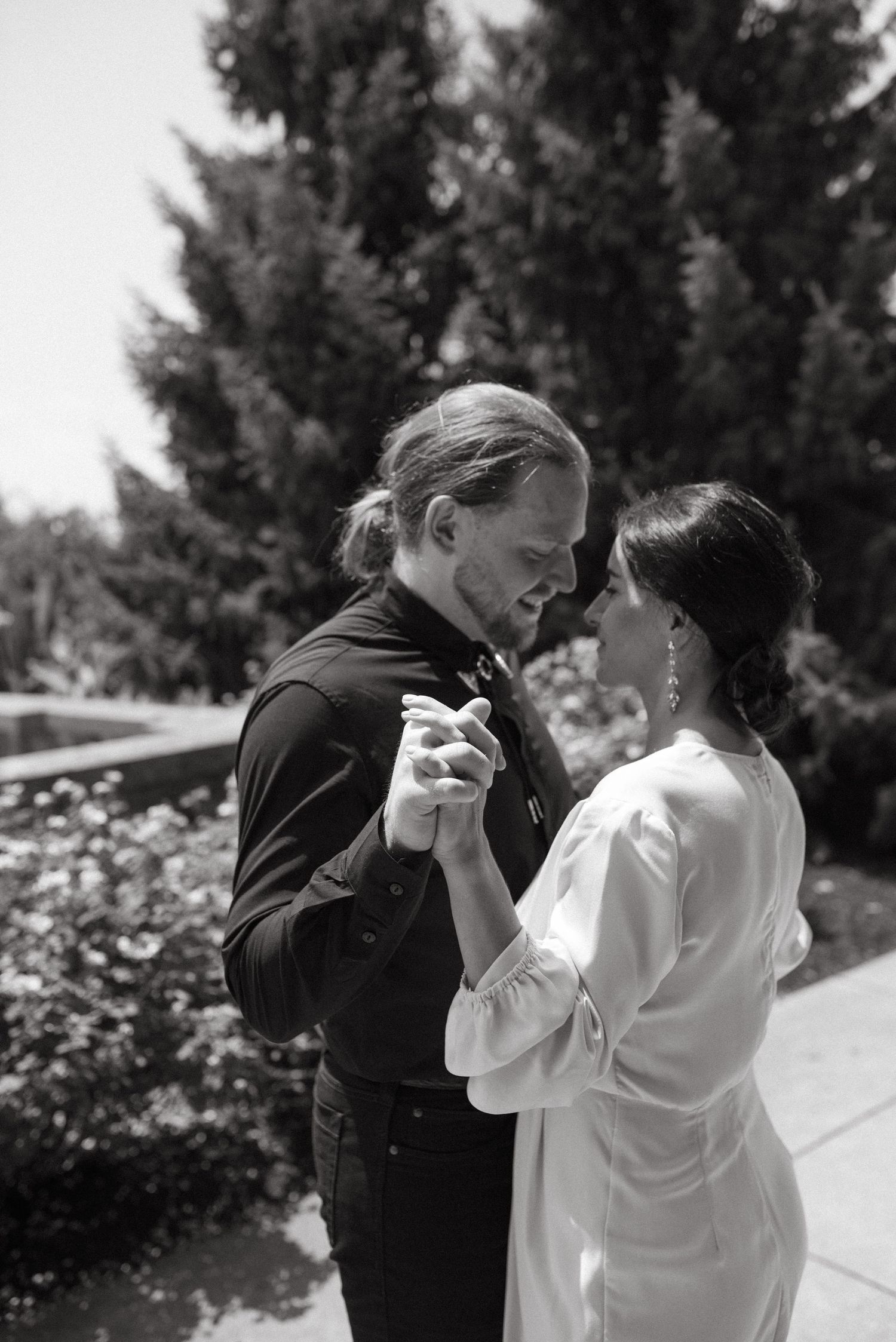 A couple shares an intimate dance moment in black and white photography with garden background.