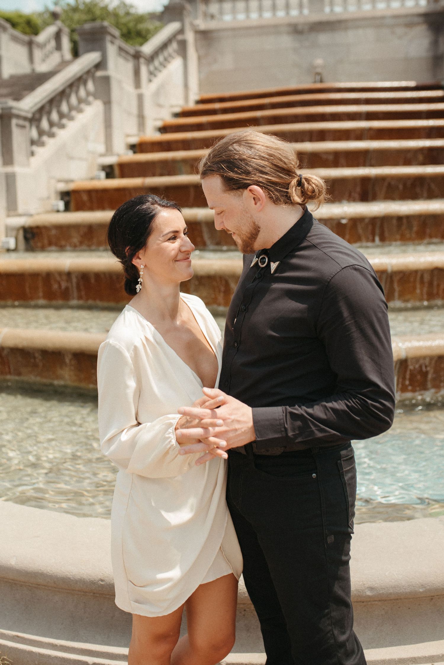 A couple shares a tender moment while dancing by a grand fountain with stone steps.