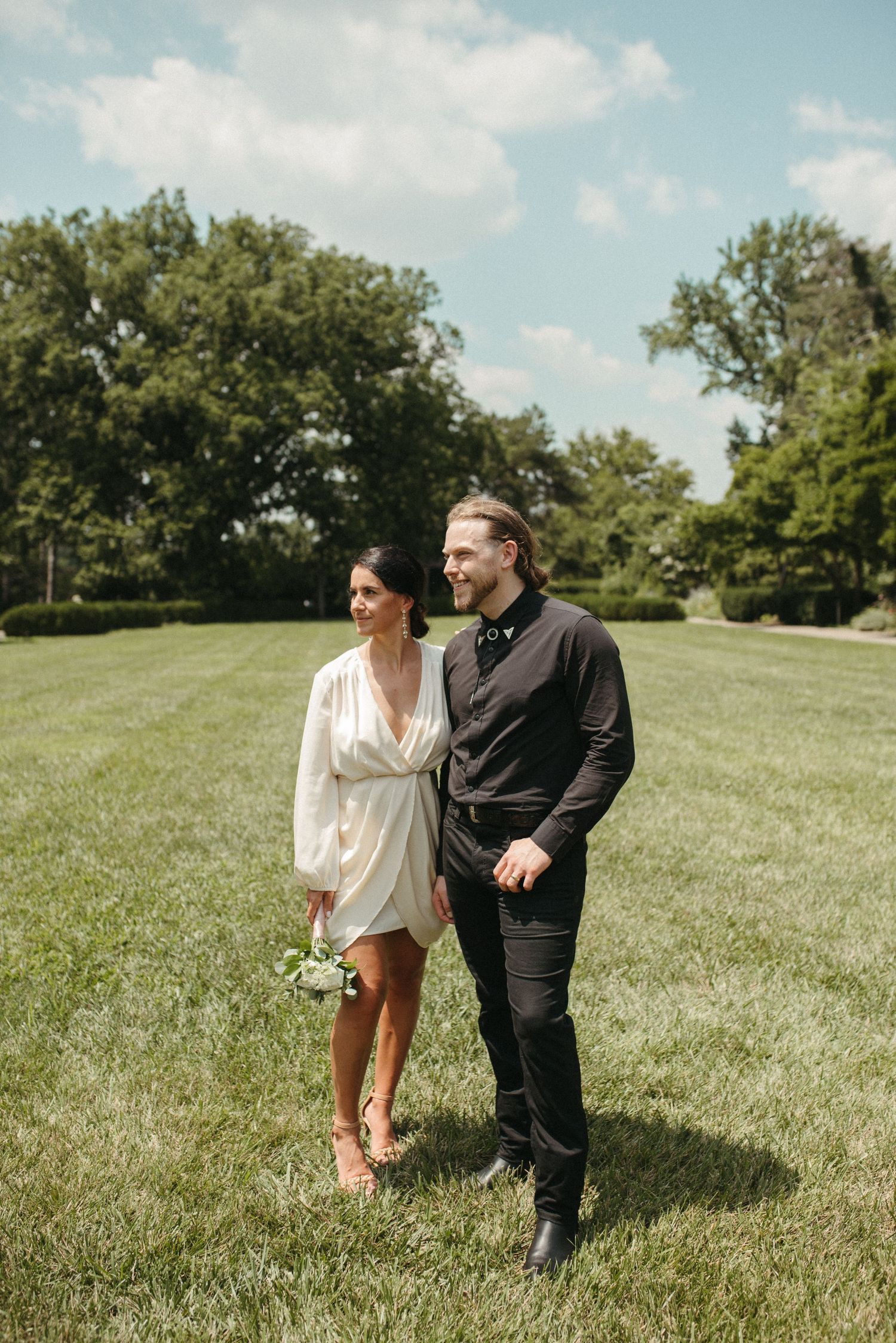 A couple strolls together across a grassy lawn on a beautiful summer day.