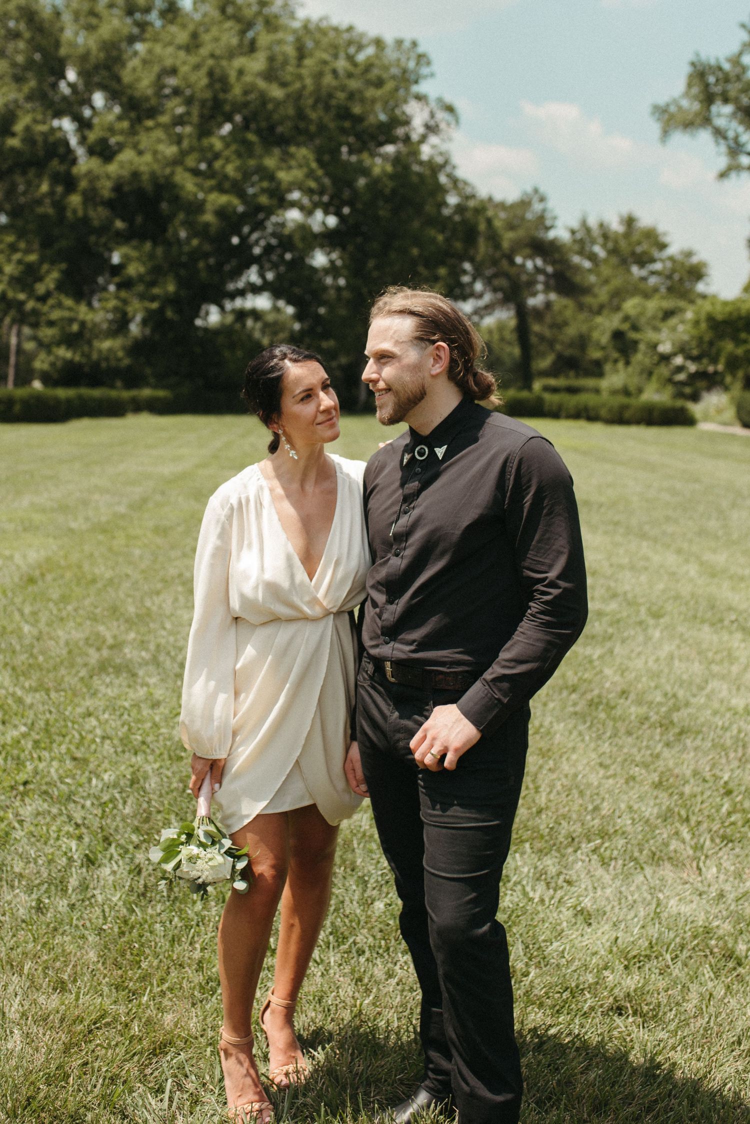 A romantic couple shares a tender moment while standing in a park on a bright summer afternoon.