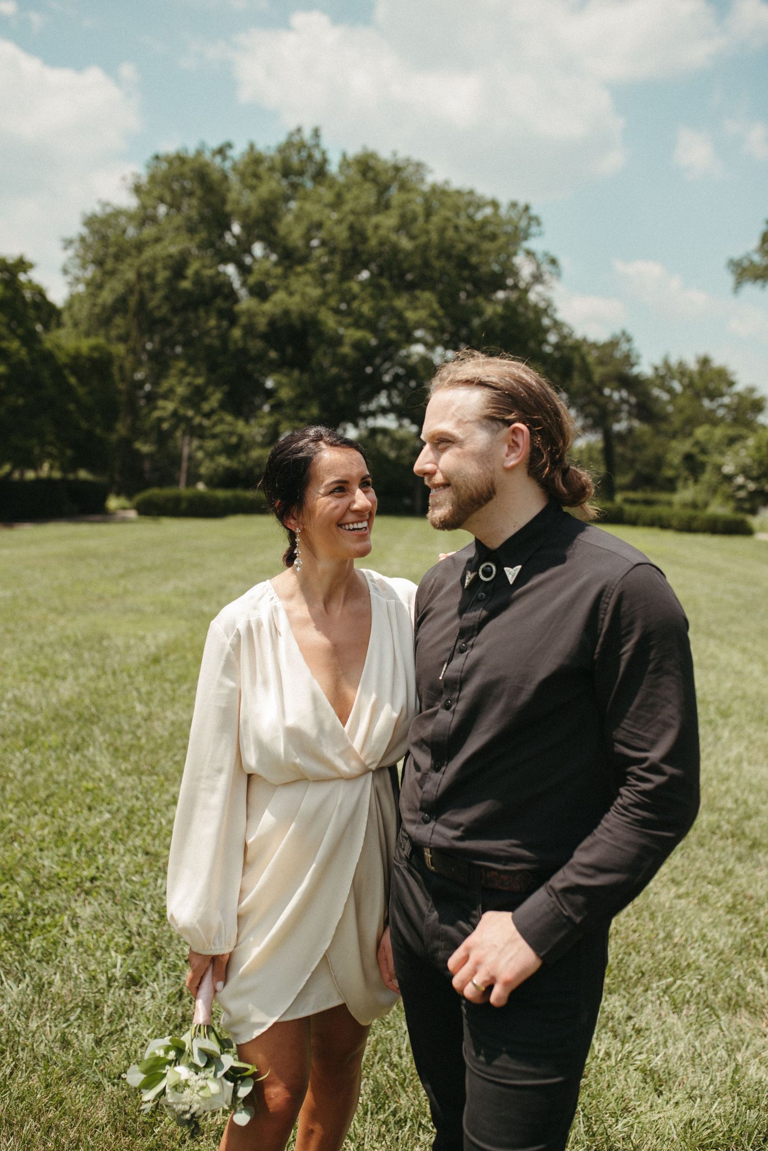 A couple shares an intimate moment while standing in a serene park setting.
