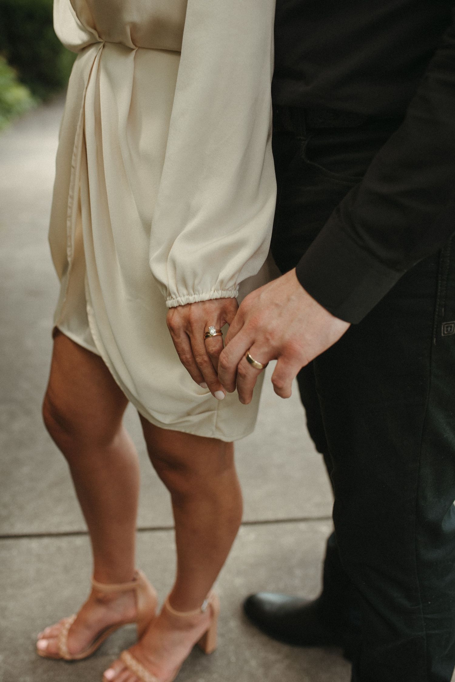 Close-up of hands with wedding rings as couple stands together on a pathway.