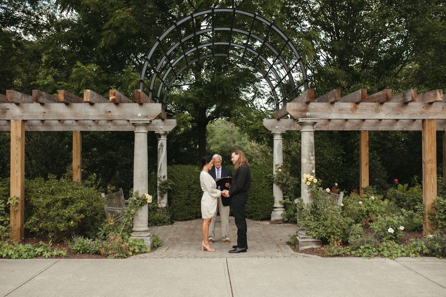 A couple shares an intimate moment during their garden wedding beneath an arched pergola.