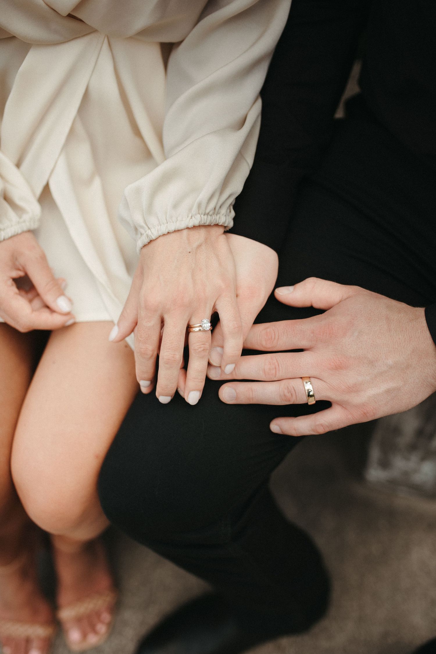 Close-up shot of hands displaying wedding rings against formal attire.