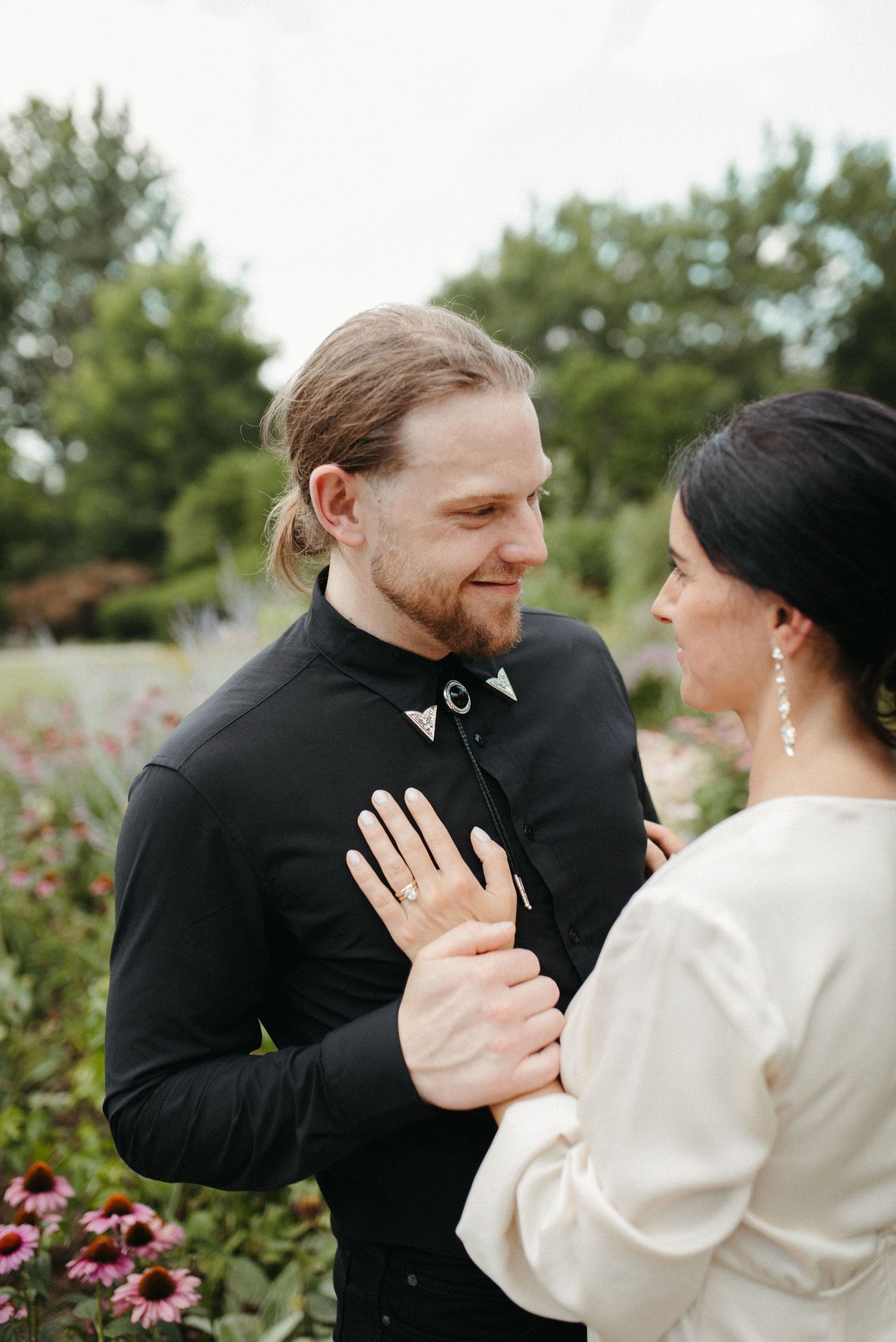 Intimate moment between couple in garden wearing black and white formal attire.