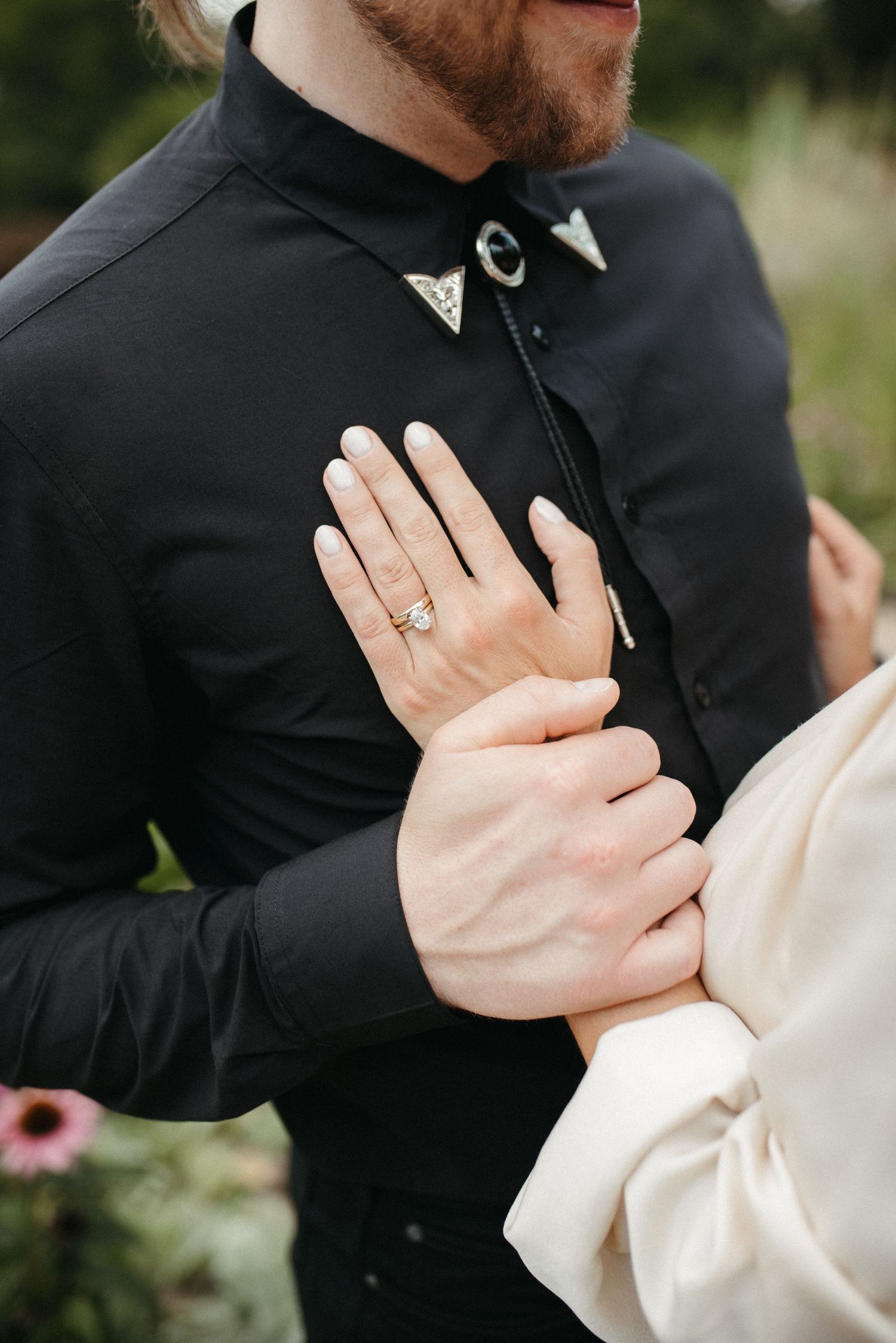 Detail shot of decorated black collar and engagement ring during couple photoshoot.