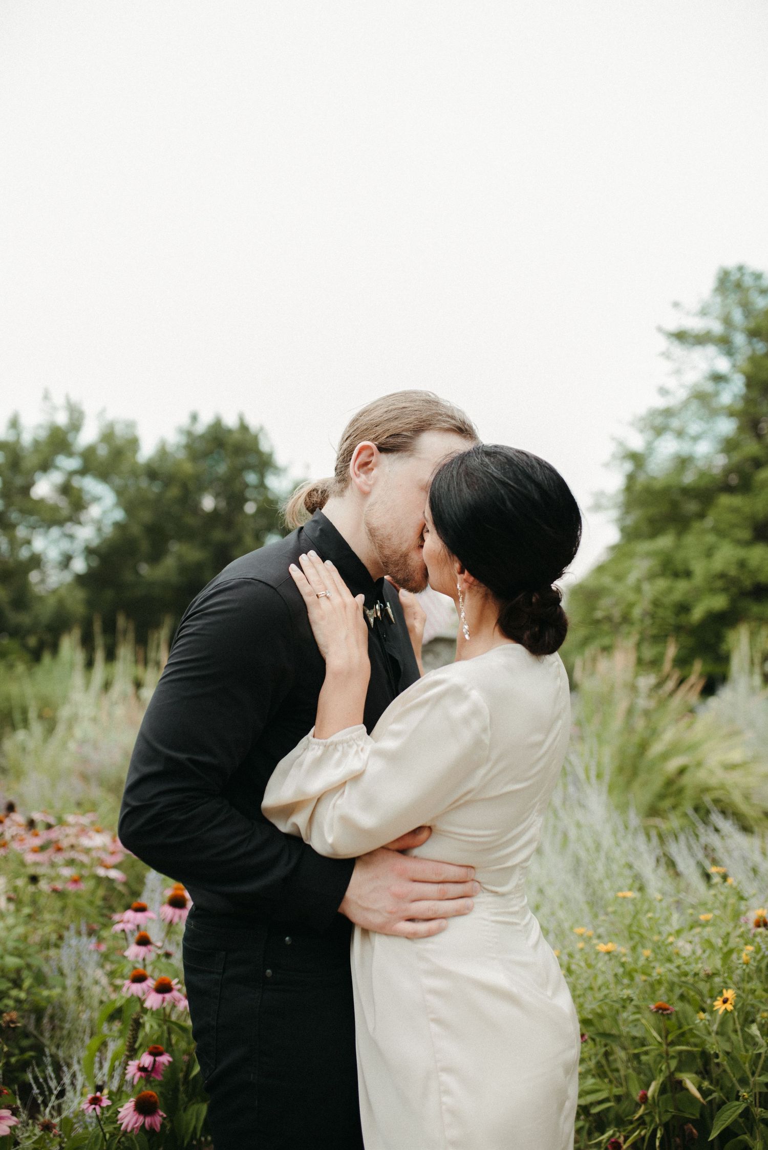 Intimate kiss shared between couple in garden setting surrounded by wildflowers.