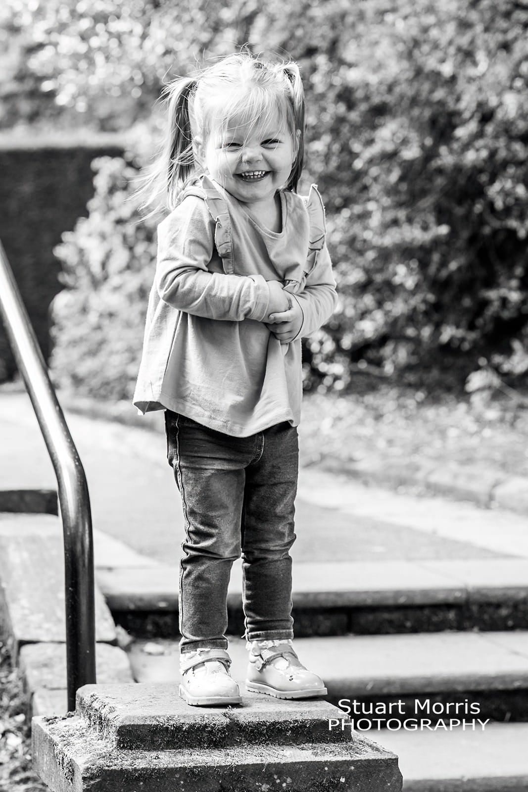 little girl with a cheeky smile stands on stone pillar. mini portrait session. Stuart Morris Photography