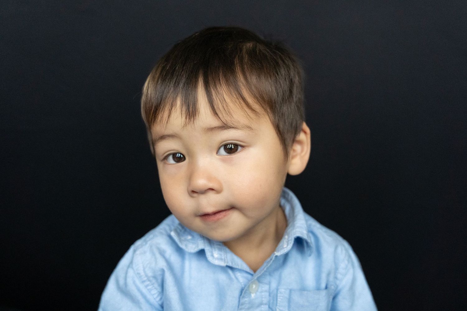 Portrait of a child in a light blue shirt against a dark background.