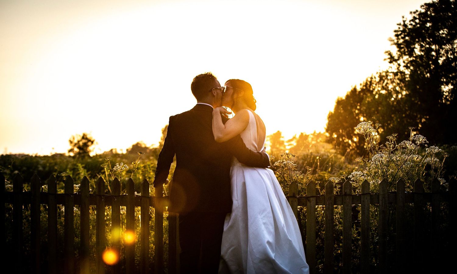 Silhouetted couple embraces during sunset with golden backlight creating a romantic atmosphere.