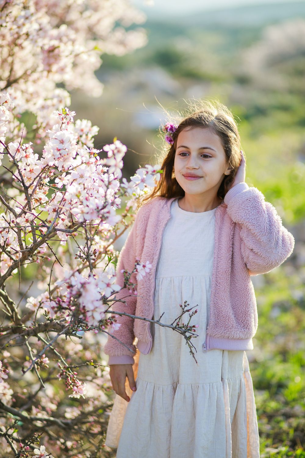A girl smiles next to a pink almond tree