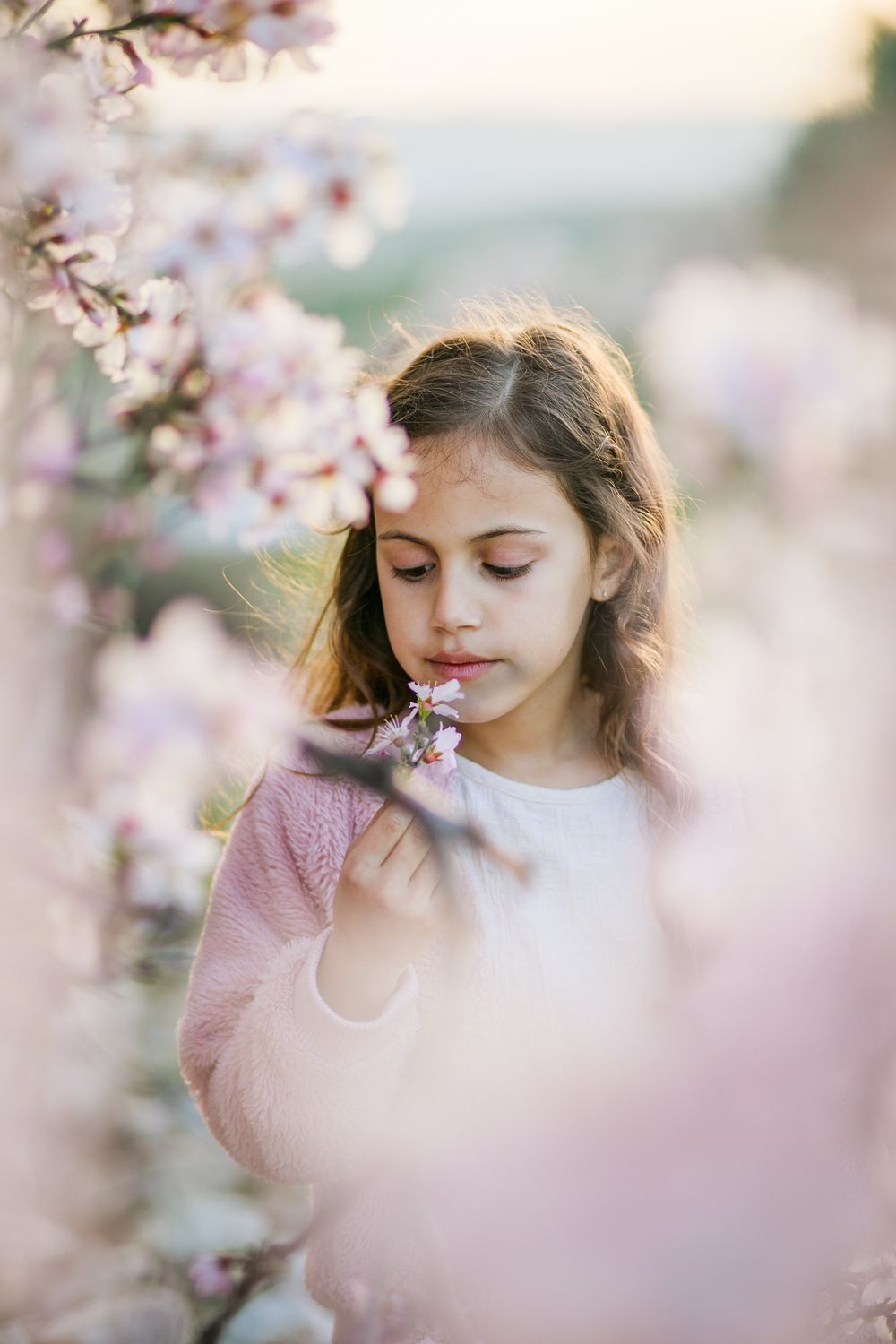 A portrait photo of a beautiful girl standing in the shade of a pink almond tree