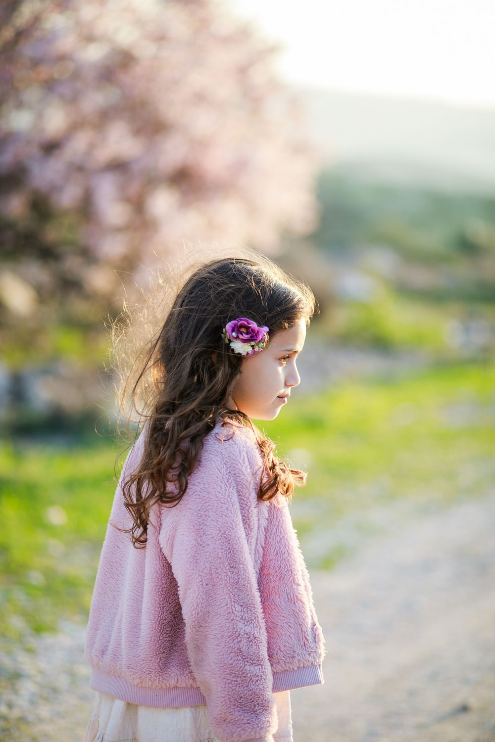 A photograph of a girl looking aside and sun touches on her hair and an almond tree in the background