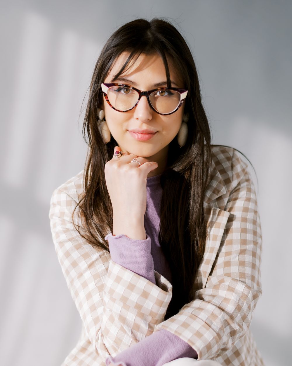 Thoughtful studio portrait featuring cat-eye glasses and beige gingham blazer.