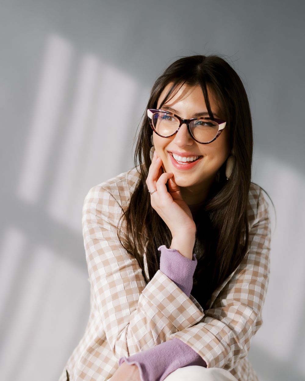 Trendy casual look with glasses showing gingham jacket and lavender sweater against a gray studio backdrop.