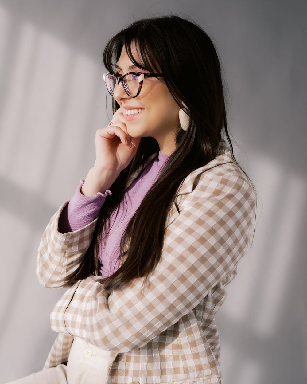 Portrait of person in checkered blazer, lilac top and glasses against light-filled backdrop.