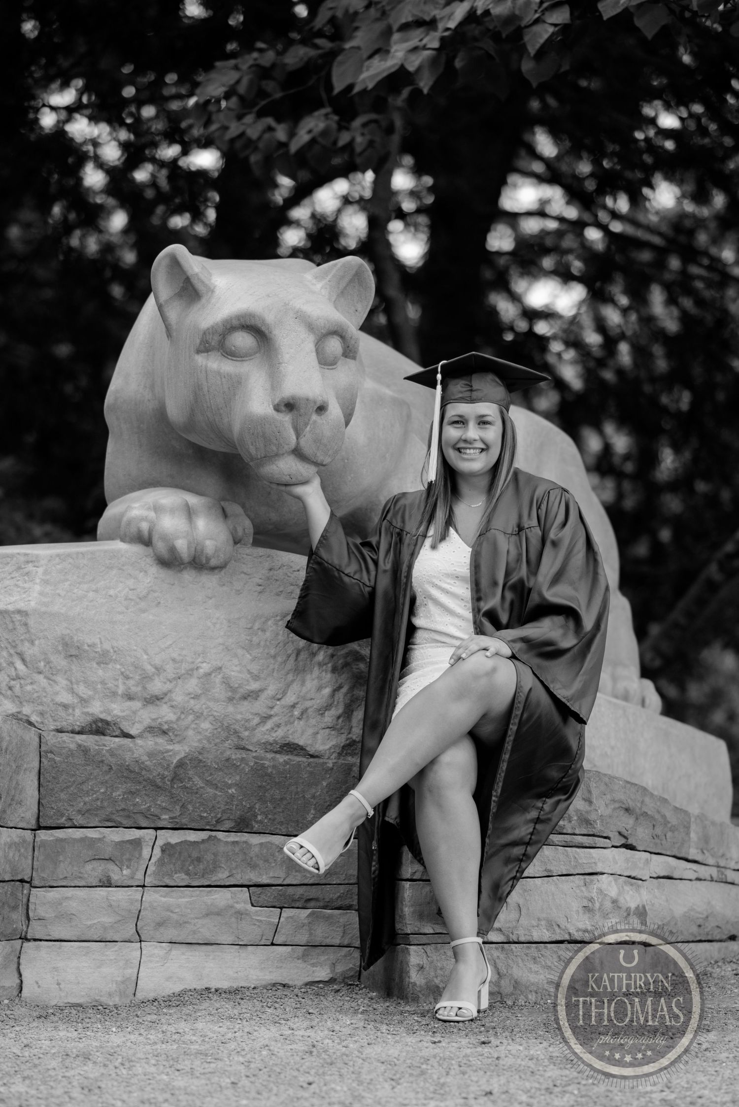 Black and white graduation photo with student posed beside Penn State's lion statue.
