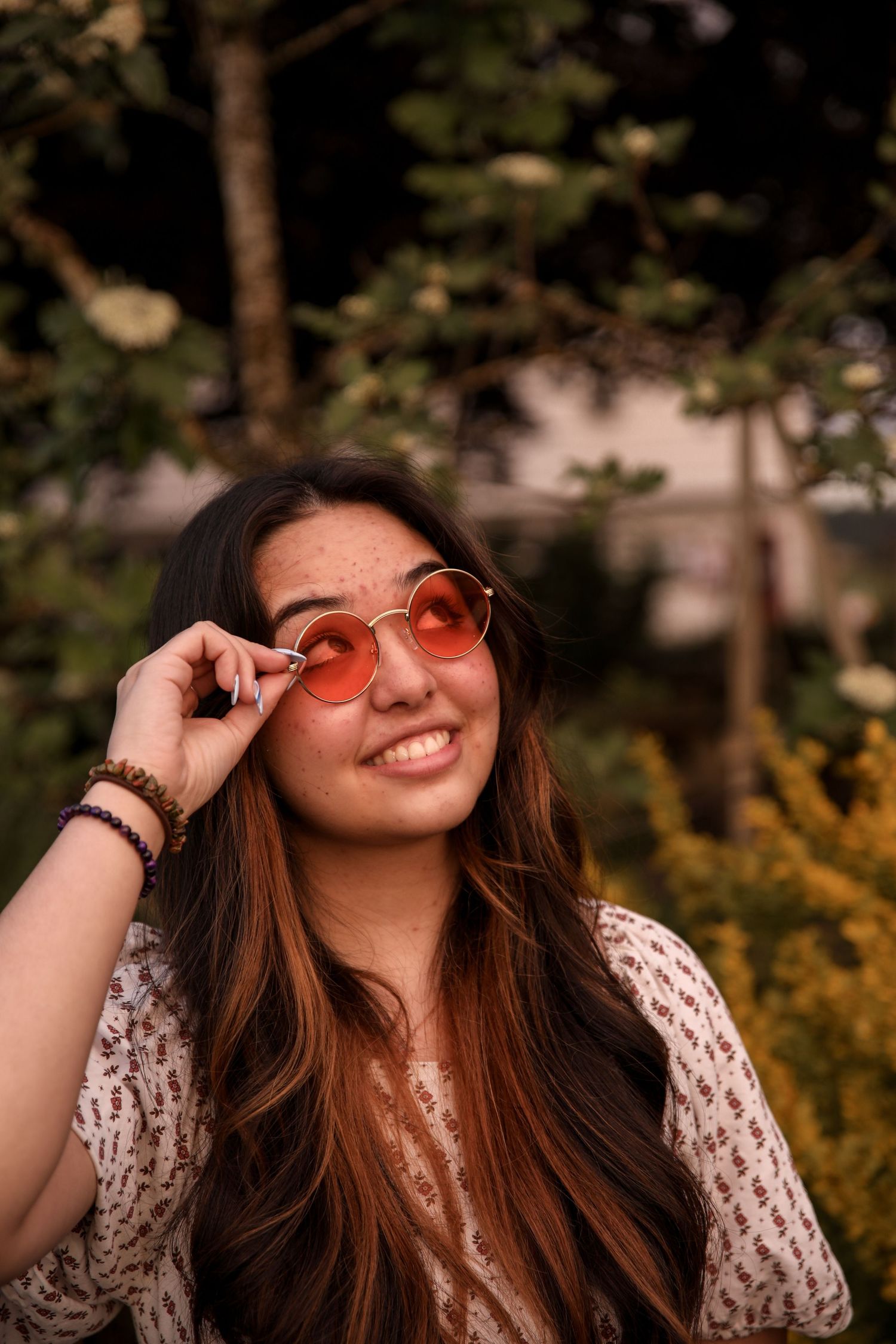 Lifestyle portrait of person wearing rose-tinted glasses and knit sweater in garden setting.