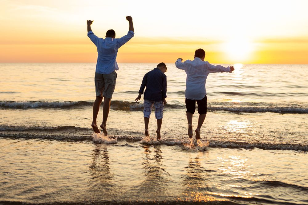 Three silhouettes jumping joyfully at beach during golden sunset.