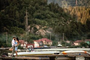 A couple shares an intimate moment on a dock overlooking mountain scenery and lakeside homes.