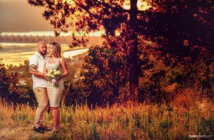 Romantic couple embracing at sunset in autumn field with golden light filtering through trees.