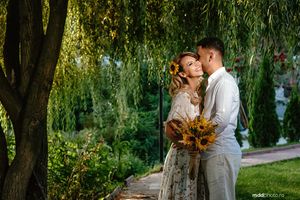 Newlyweds embracing under weeping willow tree in lush garden setting.