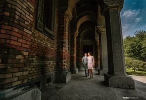 Couple walking through historic brick archway corridor in sunlight.